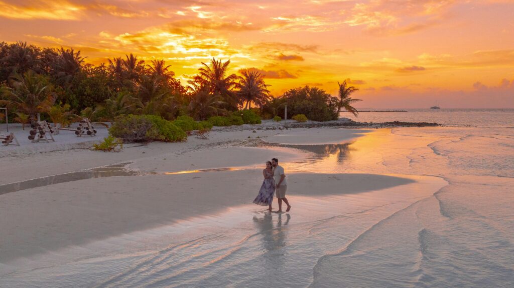 couple walking along tropical beach at sunset